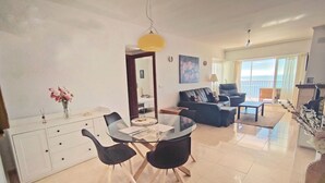 Una sala de estar moderna con una mesa de comedor de cristal, sillas negras, un sofá y un balcón con vistas.