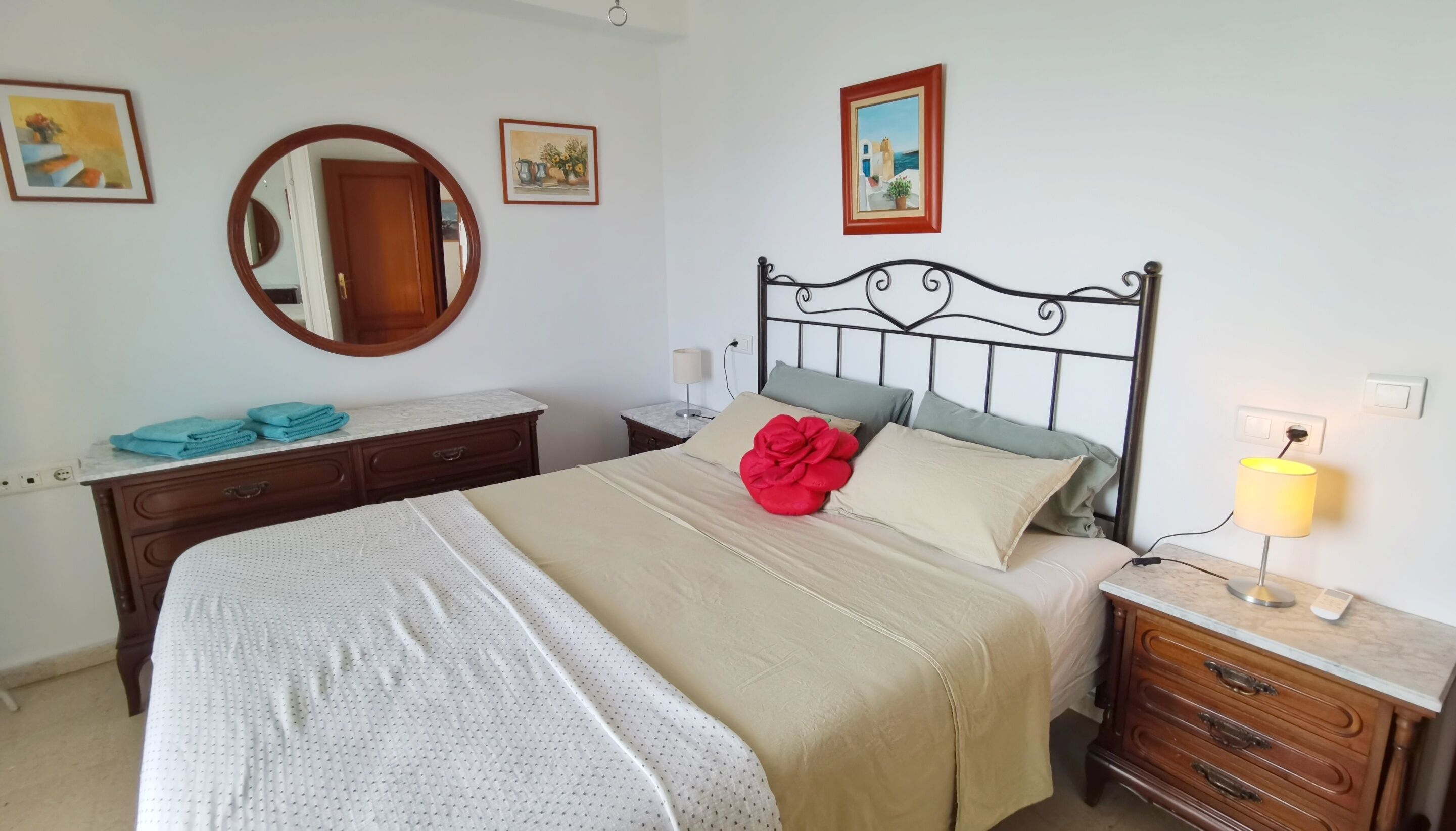 A neatly arranged bedroom with a bed, a dresser, a nightstand, a lamp, and wall art.