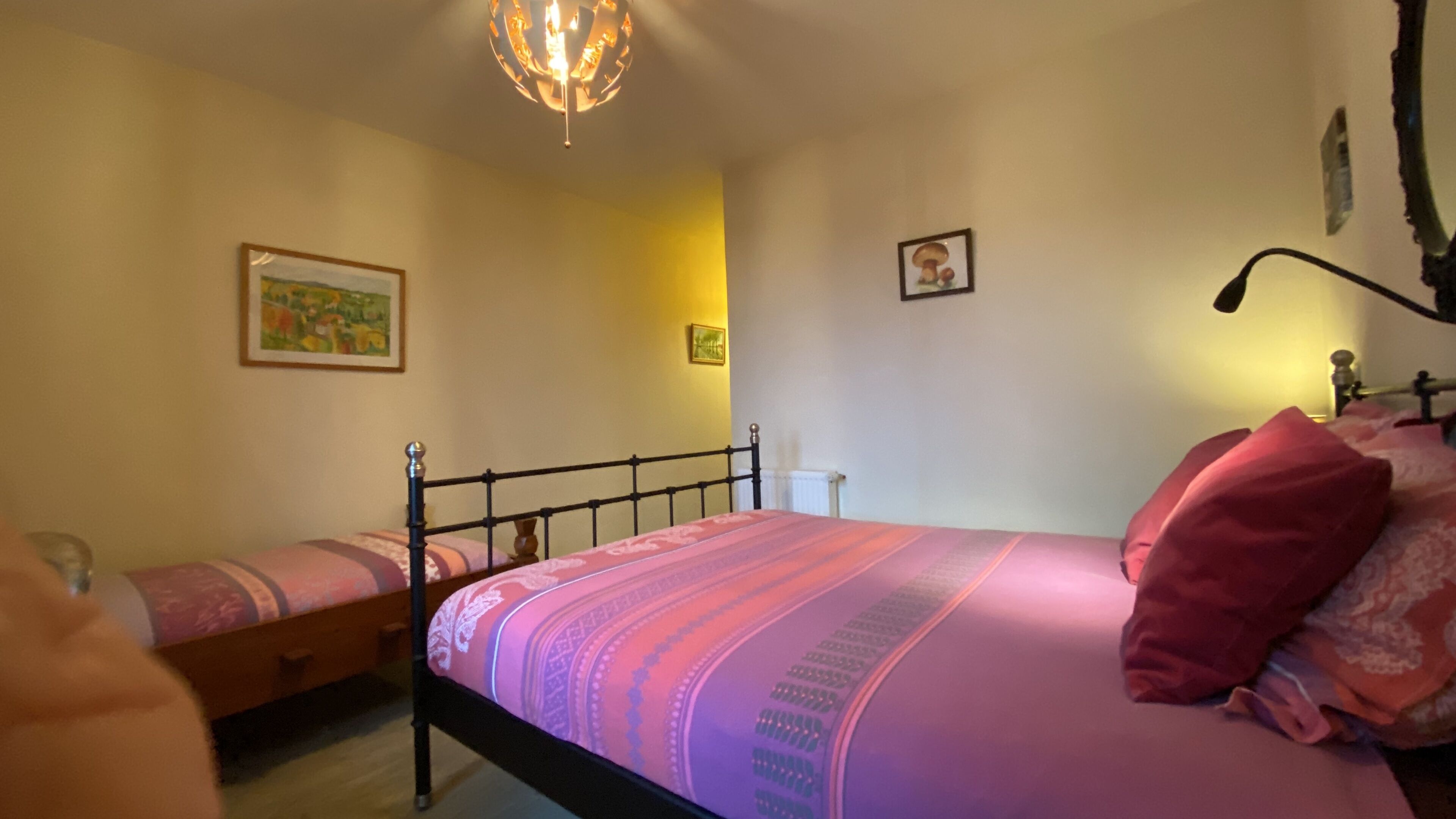 A bedroom with two beds, a chandelier, and framed pictures on the walls.