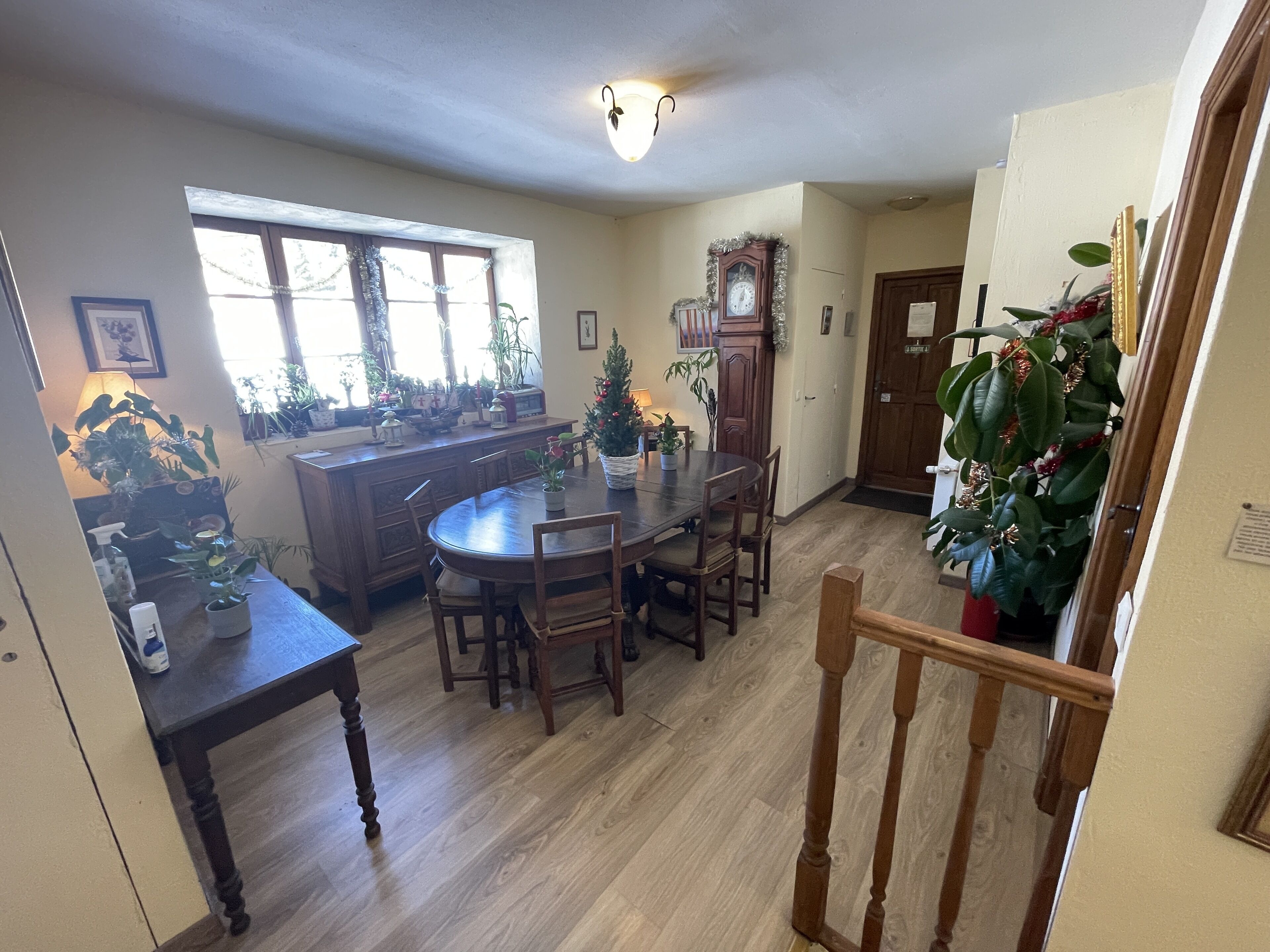 Un coin repas avec une table et des chaises en bois, une cuisine avec une fenêtre et un escalier doté d’une rampe.
