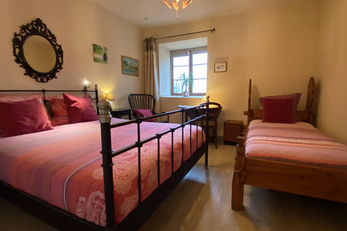 Ein Schlafzimmer mit zwei Betten, einem Sessel, einem Schreibtisch und einem Fenster mit Vorhängen.
