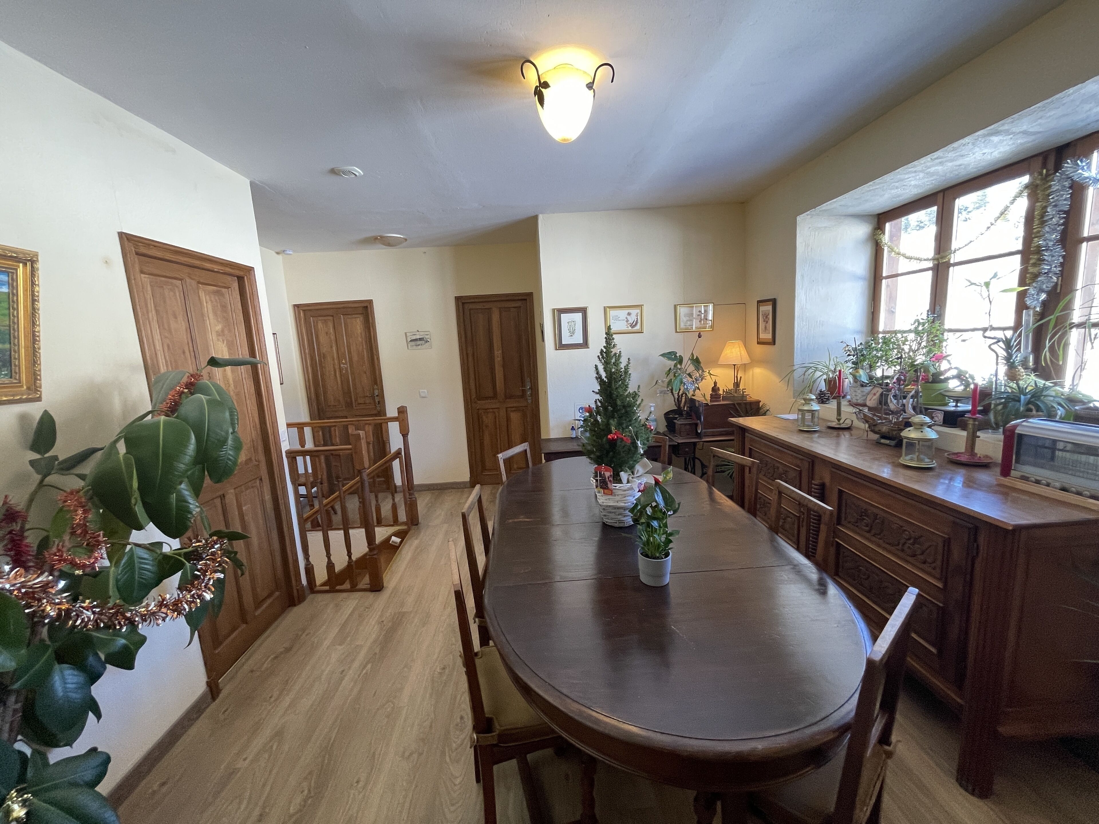 Un comedor con mesa y sillas de madera, rodeado de alacenas y un ventanal con plantas.