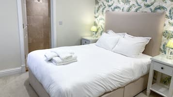 A neatly made bed with white linens and towels, a nightstand with a lamp, and a shower area with a towel rack.