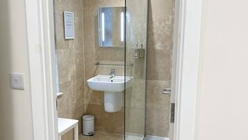 Baño con cabina de ducha de vidrio, lavamanos y espejo.