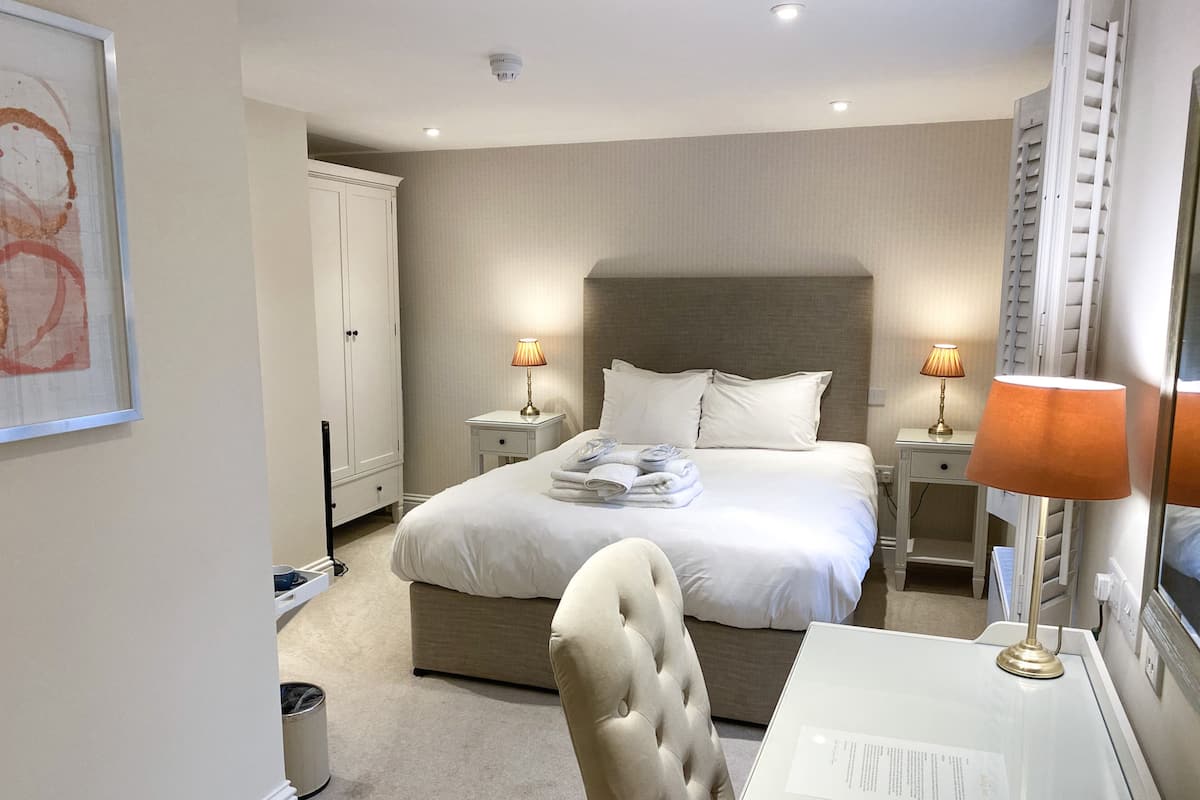 Une chambre d’hôtel avec un grand lit, deux tables de chevet avec des lampes, une chaise et un bureau avec une lampe.