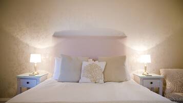 A neatly made bed with white bedding and a tree-patterned pillow, flanked by two bedside tables with lamps, in a room with patterned wallpaper.
