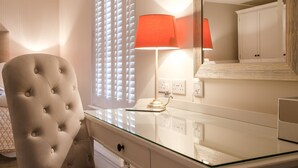 A hotel room with a tufted armchair, a glass-top desk, a red lamp, and a large mirror reflecting a wardrobe. - The Rising Sun (Bristol)
