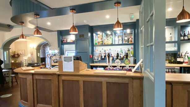 A bar area with wooden counters, copper pendant lights, and shelves stocked with bottles. - The Rising Sun (Bristol)