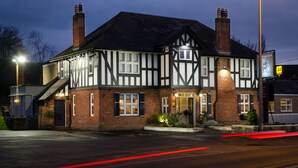 A traditional Tudor-style building with a steeply pitched roof, multiple chimneys, and a well-lit entrance. - The Rising Sun (Bristol)