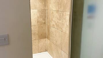 A small, enclosed shower area with beige tiles and a white floor.