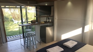 Un dormitorio con cama, escritorio, dos taburetes y una pequeña cocina.