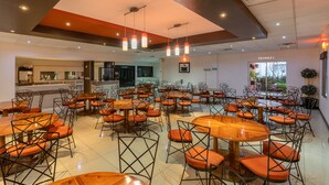A spacious dining area with multiple tables and chairs, a kitchen in the background, and a view of the outdoors. - Hotel Sntenario (Chihuahua)