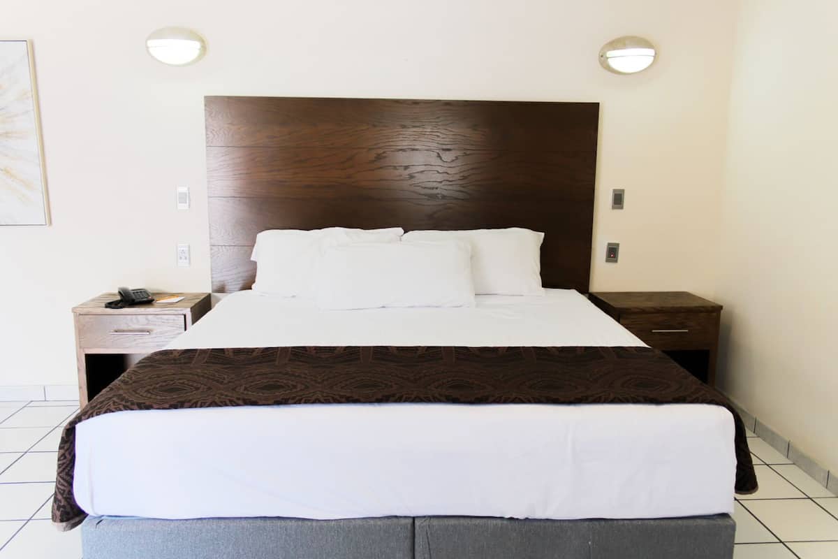 A hotel room with a large bed, a wooden headboard, two bedside tables, and a telephone on one of the tables.