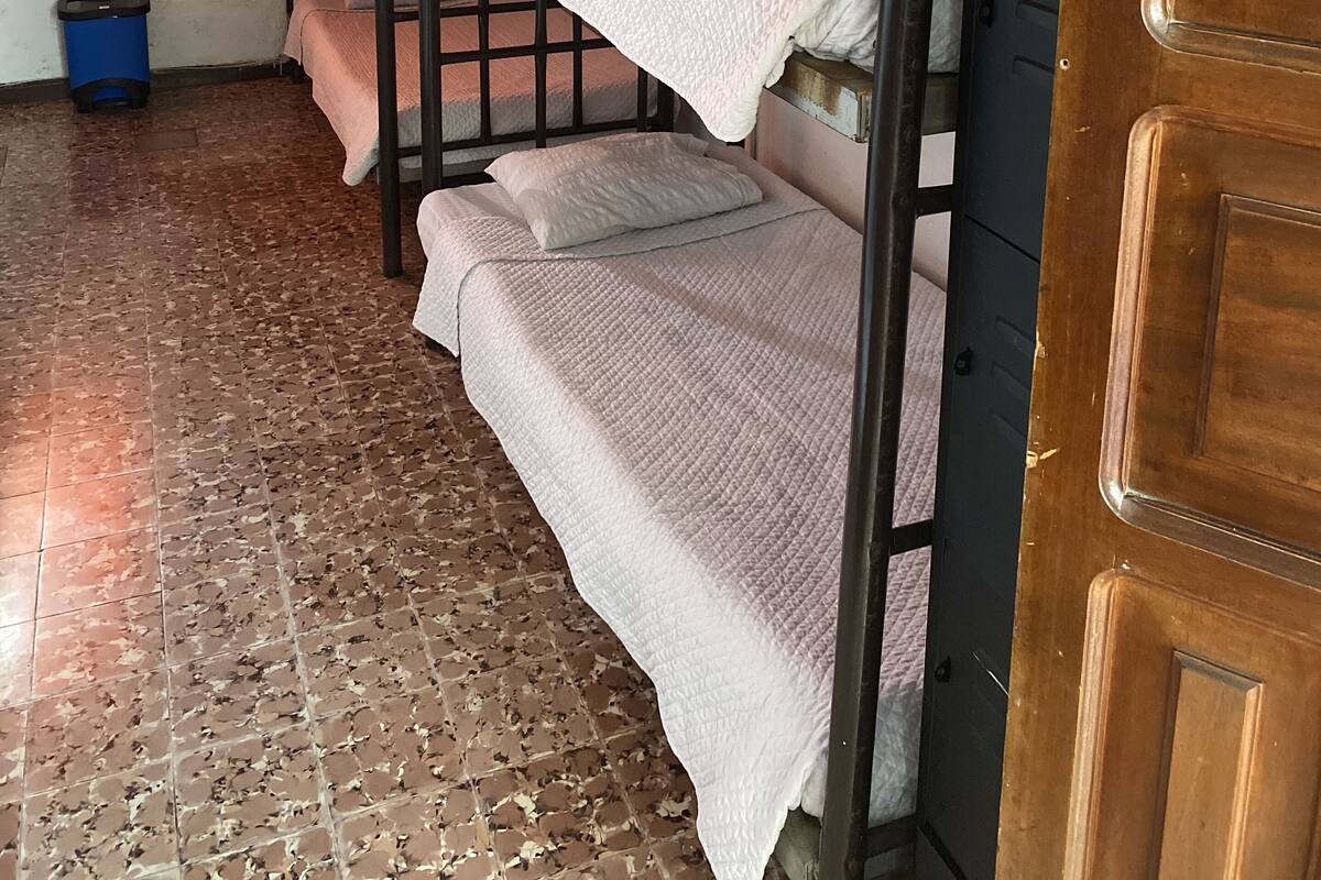 Ein Schlafsaalzimmer mit Etagenbetten, einem an der Wand befestigten Fernseher, einer Tür und einem Fenster mit orangefarbenem Vorhang.