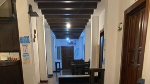 A hallway with a tiled floor, wooden benches, a reception desk, and a door. - Feathers Hotel and Lounge - Hostel (Antigua Guatemala)