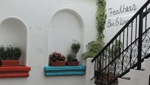 A staircase with a black wrought iron railing leading to a landing. There are potted plants on the landing and along the wall, and a sign that reads "Feathers Bar & Lounge". - Feathers Hotel and Lounge - Hostel (Antigua Guatemala)