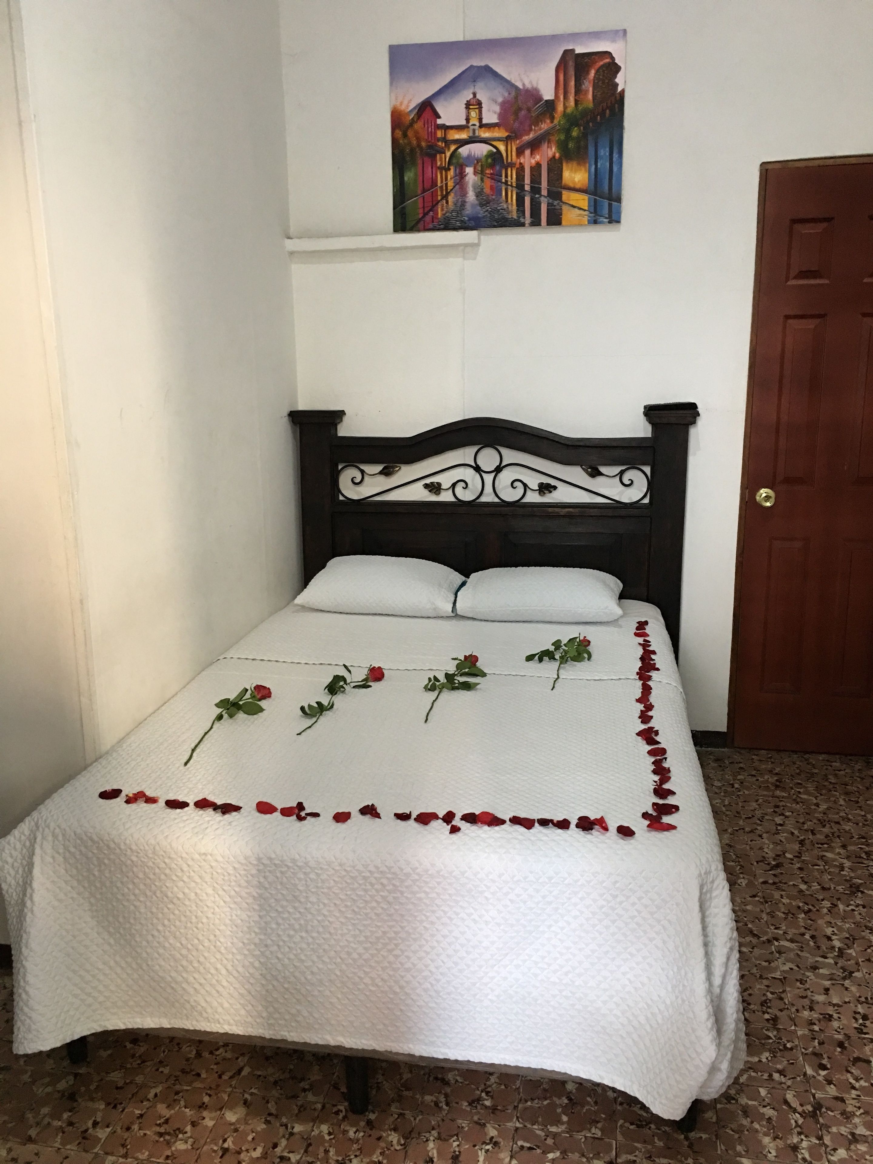 Un lit bien fait, recouvert d’une courtepointe blanche, avec une tête de lit décorative et un tableau accroché au-dessus.