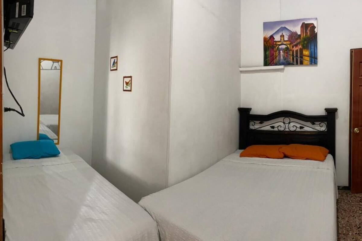 Ein Zimmer mit zwei Einzelbetten, einer Holztür, einem Spiegel und einem Bild an der Wand.