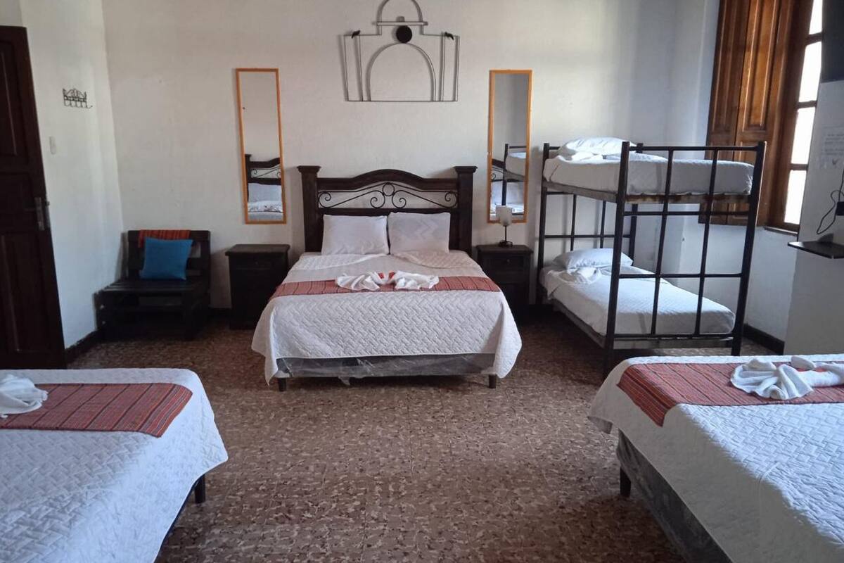 Ein Zimmer mit einem großen Bett, zwei Einzelbetten, einem Stockbett, einem Sessel und einem Spiegel.