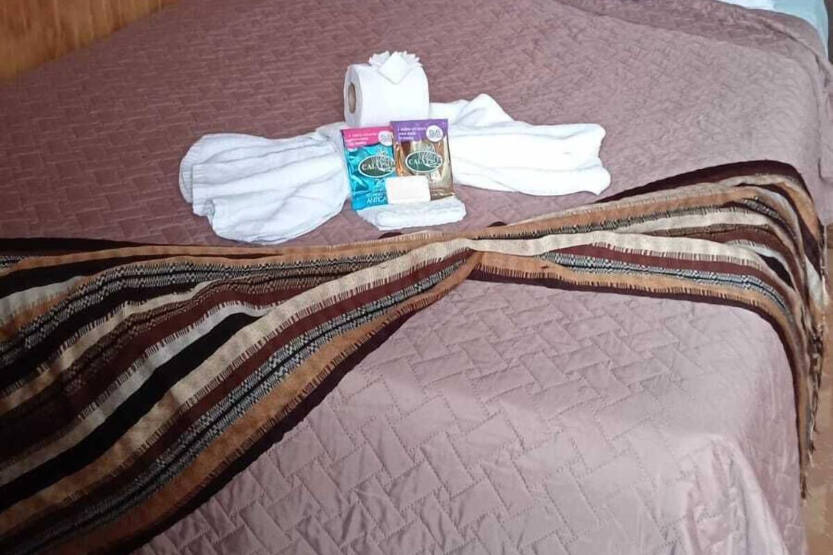 Ein ordentlich gemachtes Bett mit einer gemusterten Decke, einem Kopfkissen und einem aufgerollten Handtuch.