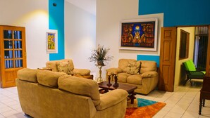 A living room with two beige sofas, a coffee table, and a rug. There is a bookshelf, a painting, and a door leading to another room. - Hotel Fontana (Managua)