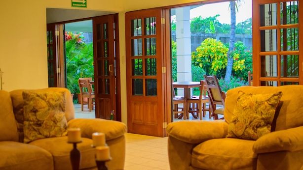 A hotel lobby with two sofas, a wooden table, and a view of a garden through open doors. - Hotel Fontana (Managua)