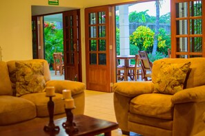 A hotel lobby with two sofas, a wooden table, and a view of a garden through open doors. - Hotel Fontana (Managua)