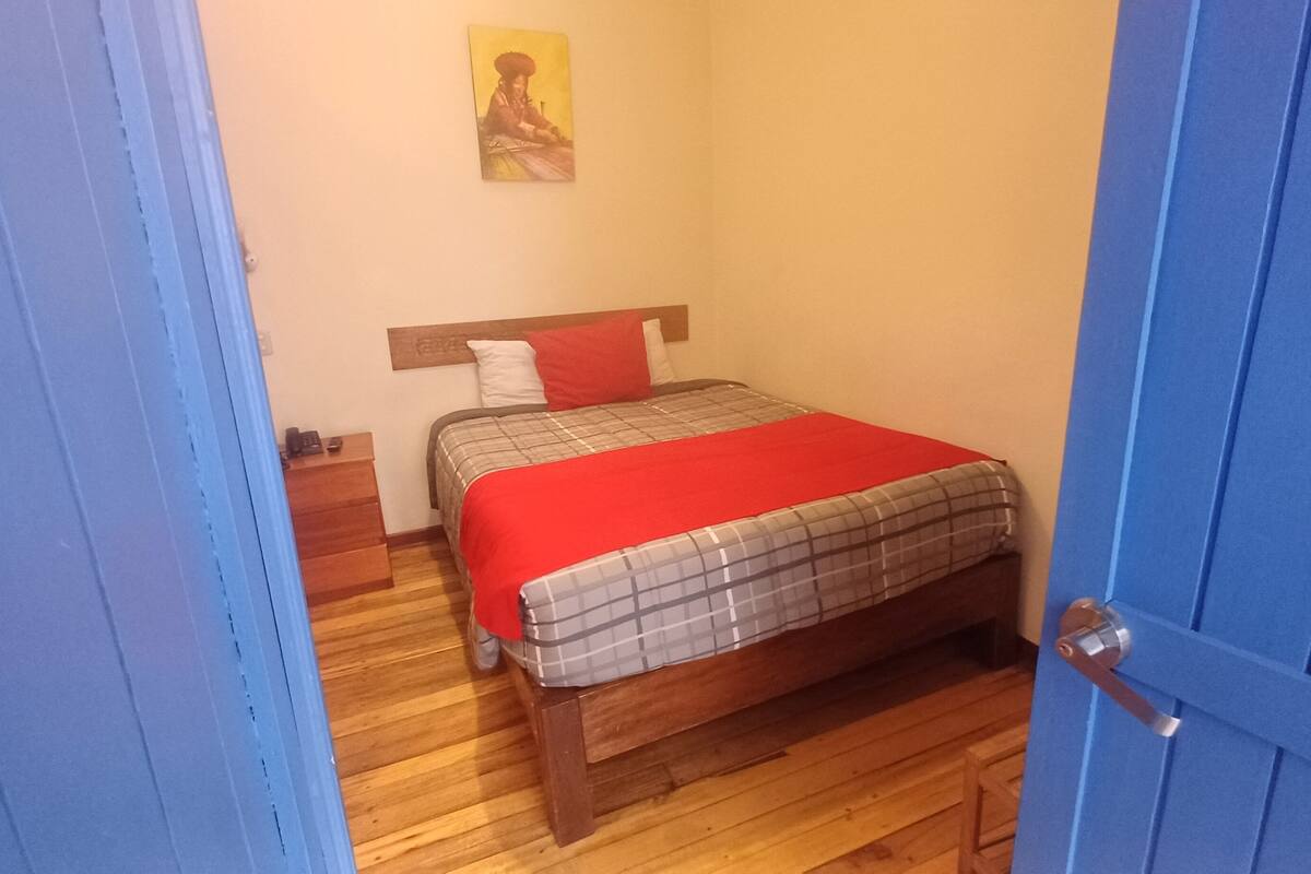 Un dormitorio con una cama de madera, un edredón a cuadros rojo y gris, y una almohada roja.