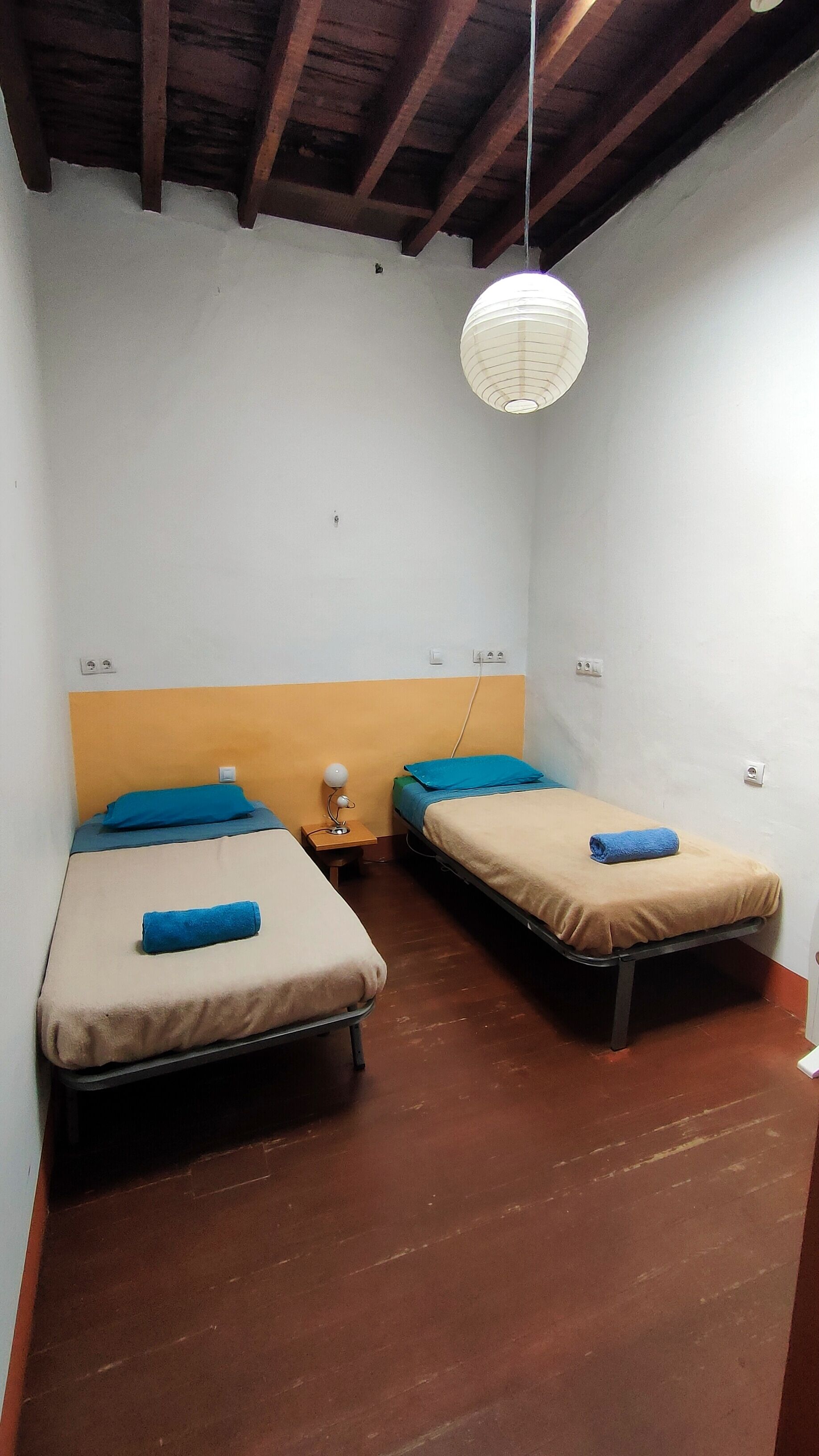Un alojamiento pequeño, de una sola habitación, con dos camas, una mesita de noche y una lámpara colgante.