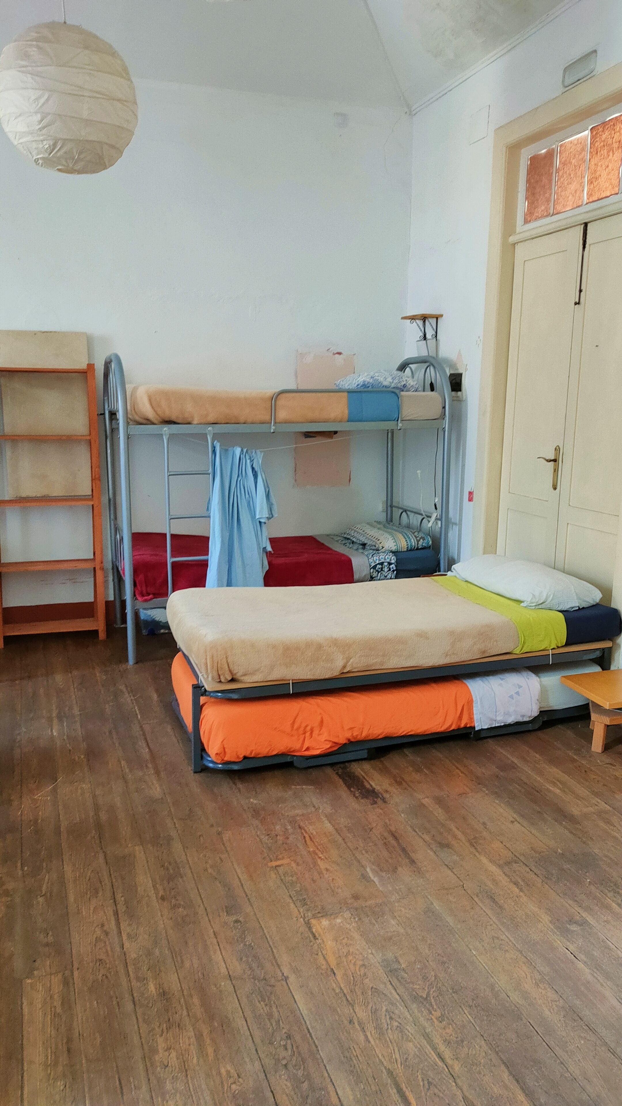 Een studentenkamer met stapelbedden, een houten vloer, een kledingkast en een hanglamp.