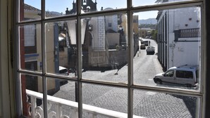 Vista de una calle a través de una ventana, con pavimento de adoquines, edificios y vehículos estacionados.
