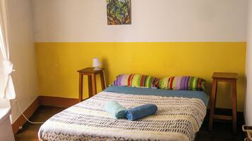 Un dormitorio con cama, mesita de noche, lámpara colgante y un cuadro en la pared.
