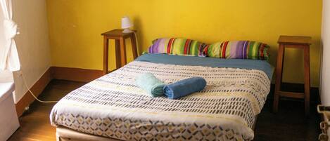 Een slaapkamer met een bed, een nachtkastje, een hanglamp en een schilderij aan de muur.