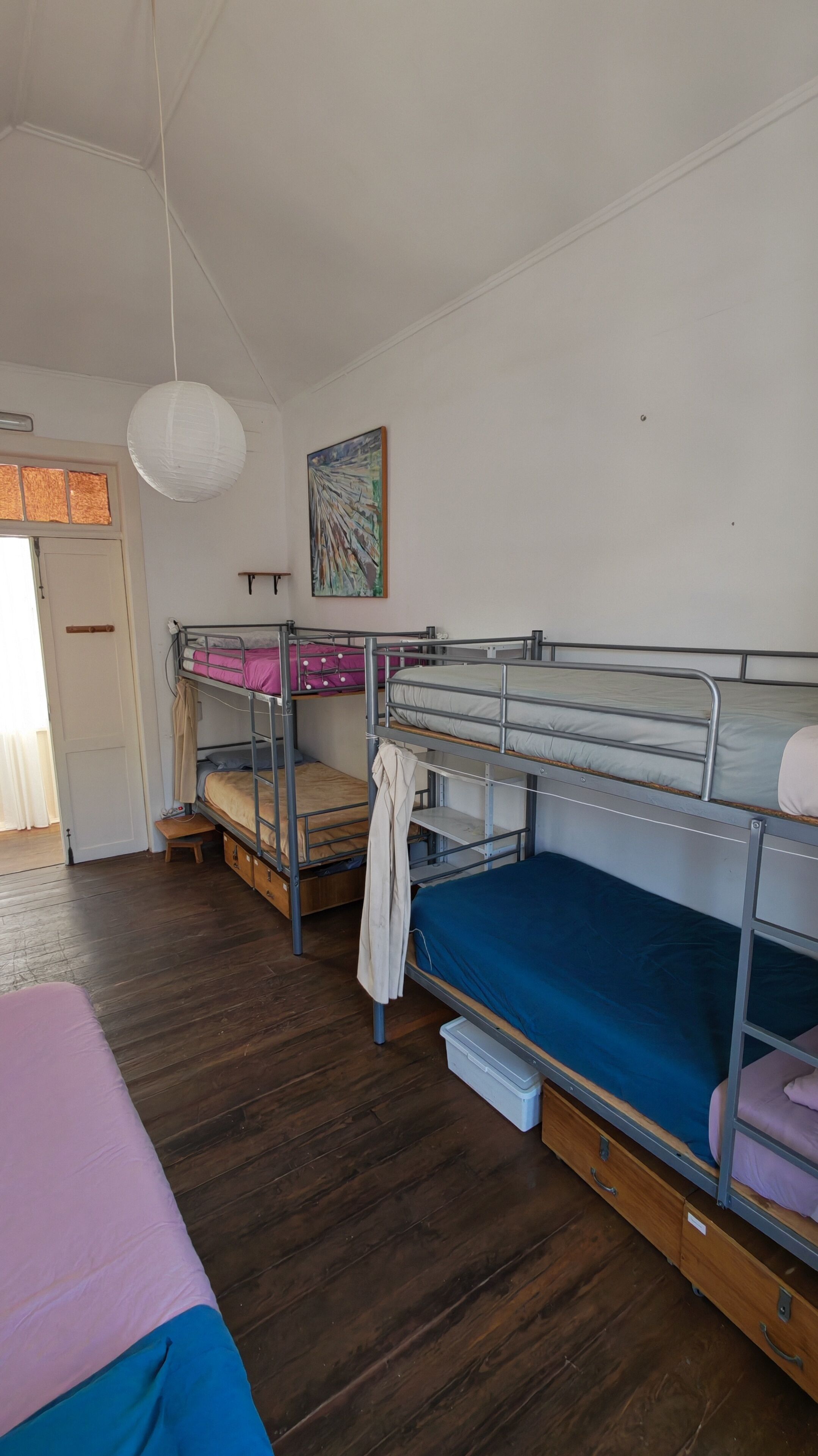 Een slaapzaal met stapelbedden, een houten vloer, een witte deur en een schilderij aan de muur.