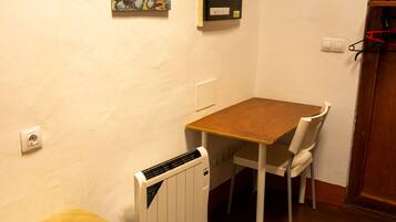 A small room with a bed, a table, a chair, a radiator, and a painting on the wall.