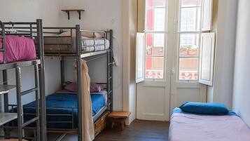 Un dormitorio con literas, una mesita pequeña y una ventana con vistas a edificios.