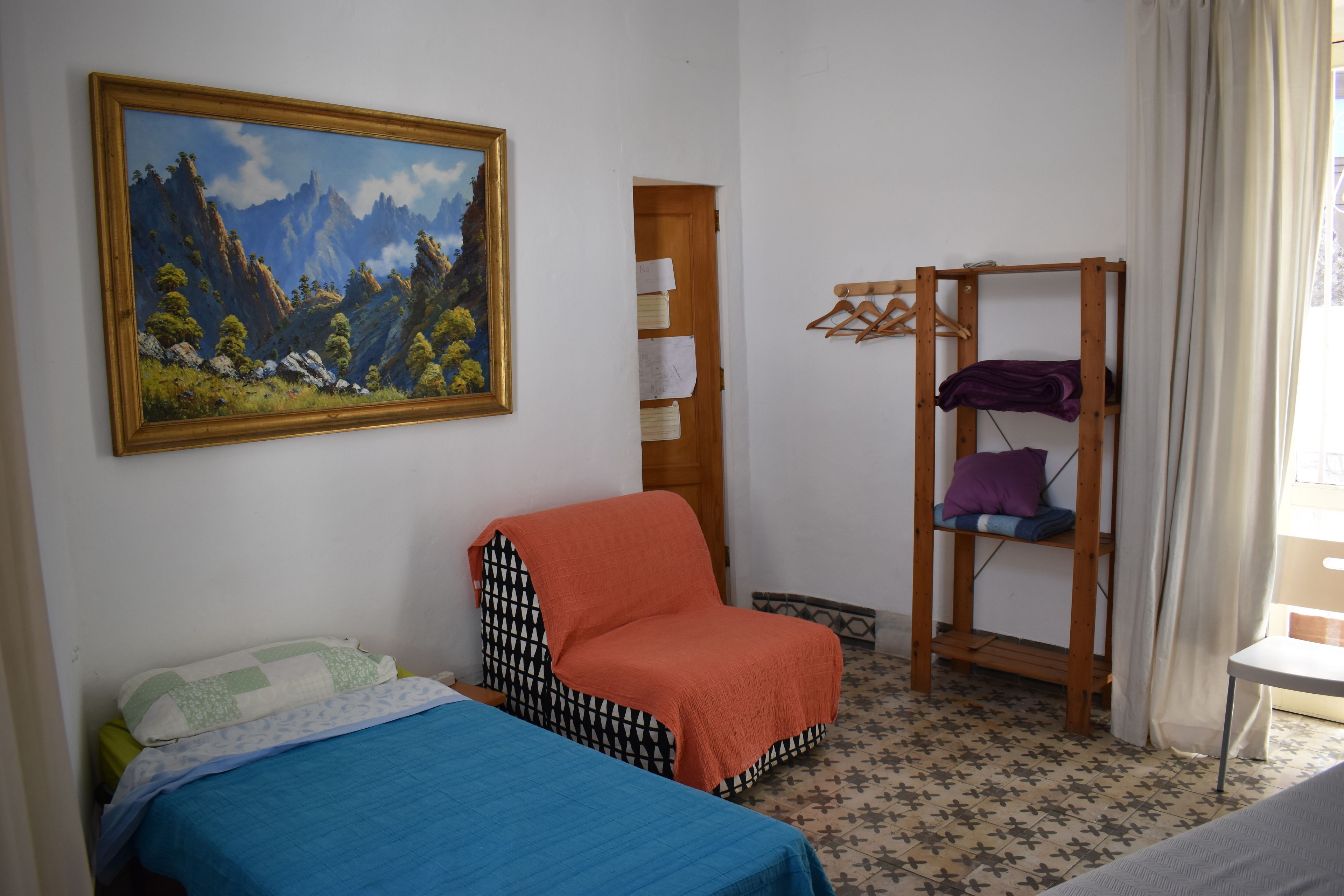 Una habitación con dos camas, una silla, una cama nido de madera, un cuadro y un suelo estampado.