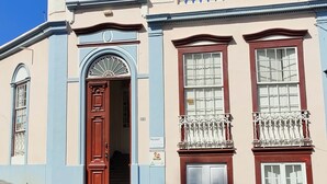 Un edificio con puerta roja, un balcón con barandilla blanca y un cartel que indica que es un albergue.