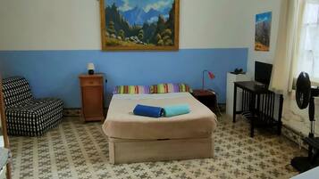 A hotel room with a bed, a chair, a desk, a lamp, and a painting on the wall.