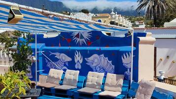 A rooftop terrace with blue and white lounge chairs, a patterned wall, and potted plants.