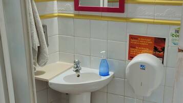 Un baño con lavamanos, inodoro y espejo. Hay una toalla colgada en la pared y un dispensador de jabón en el lavamanos.