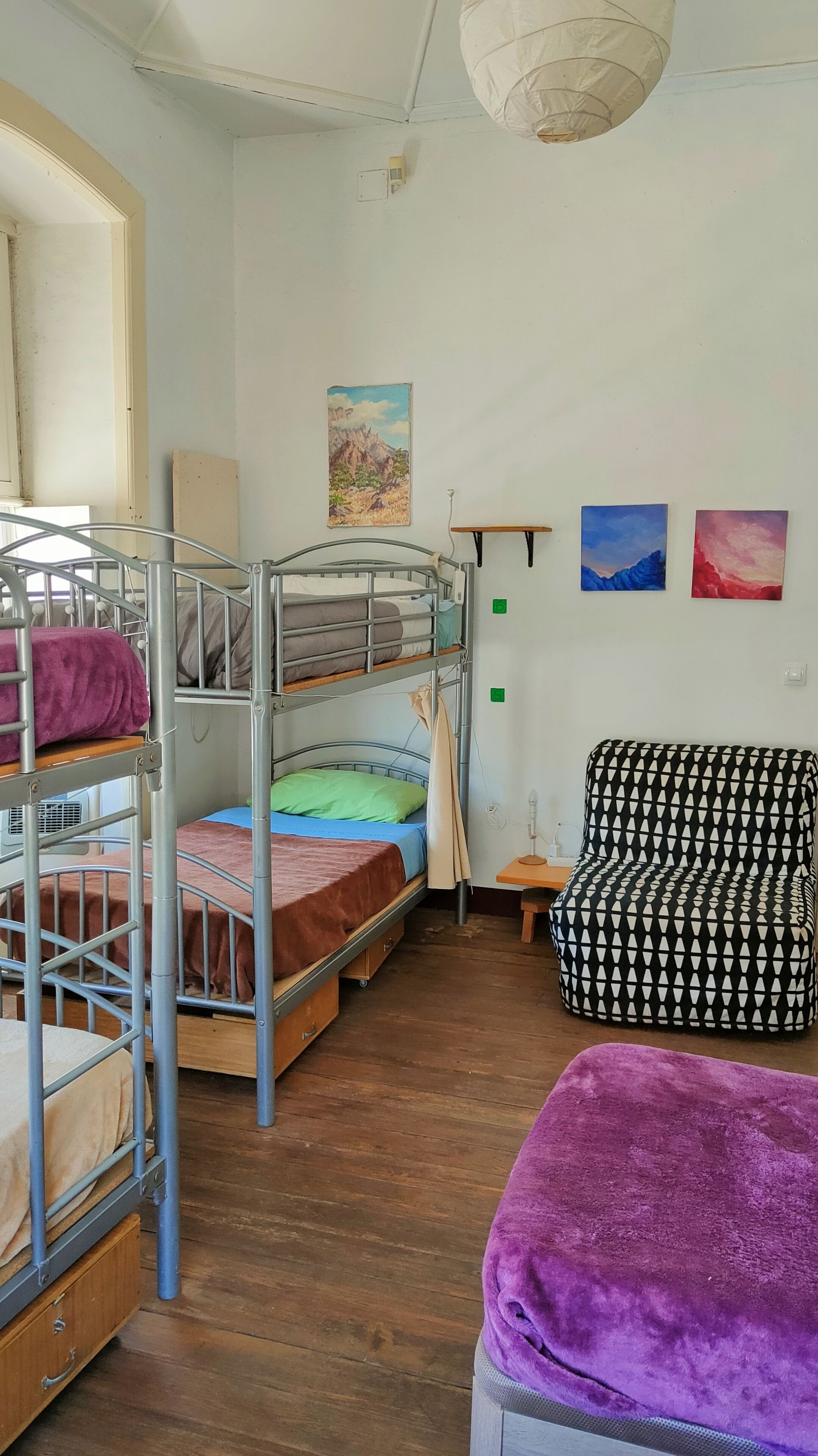 A dormitory room with bunk beds, a desk, a chair, and a purple blanket.