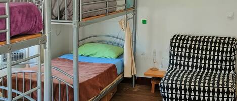 A dormitory room with bunk beds, a desk, a chair, and a purple blanket.