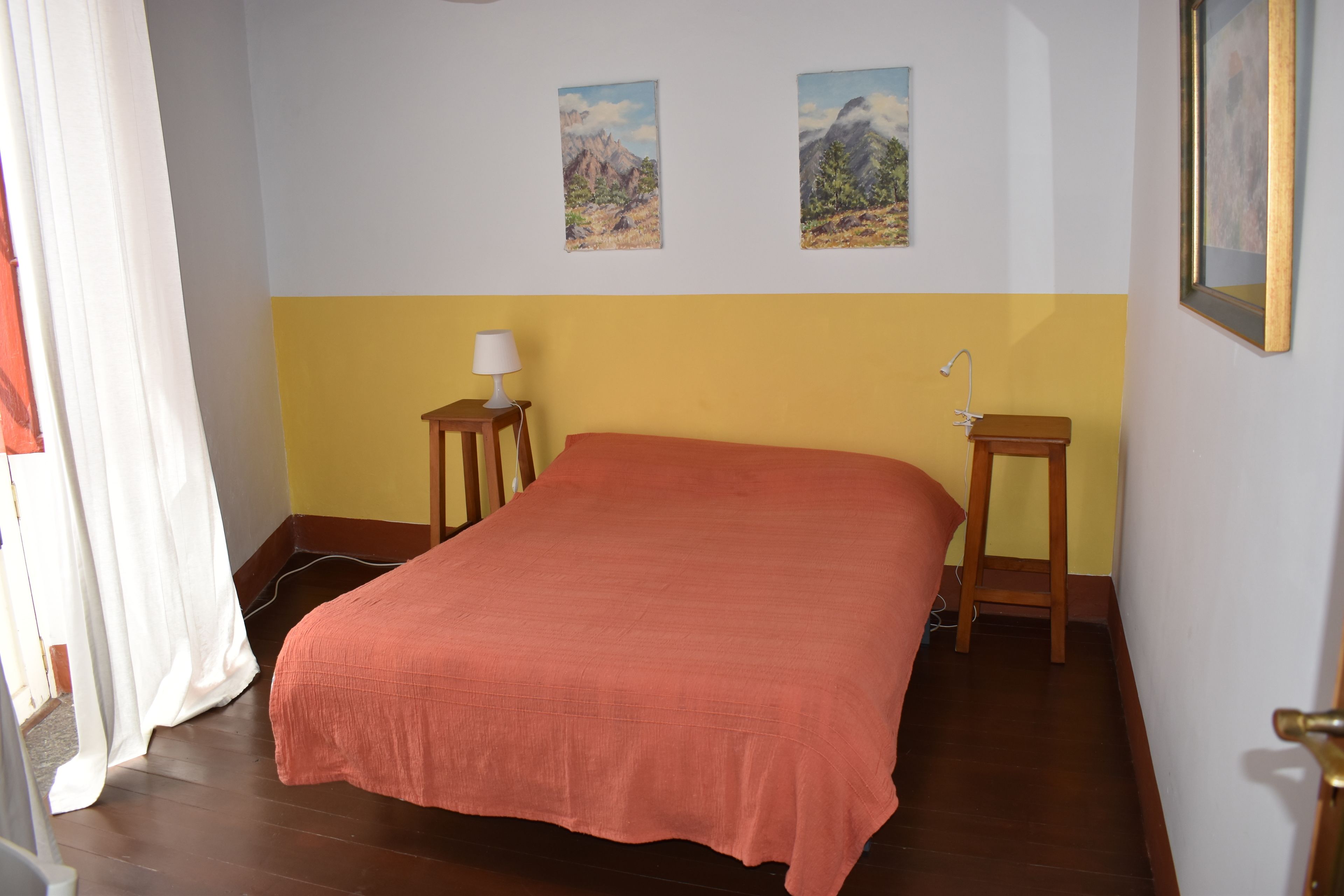 A bedroom with a bed, a nightstand, a lamp, and two paintings on the wall.