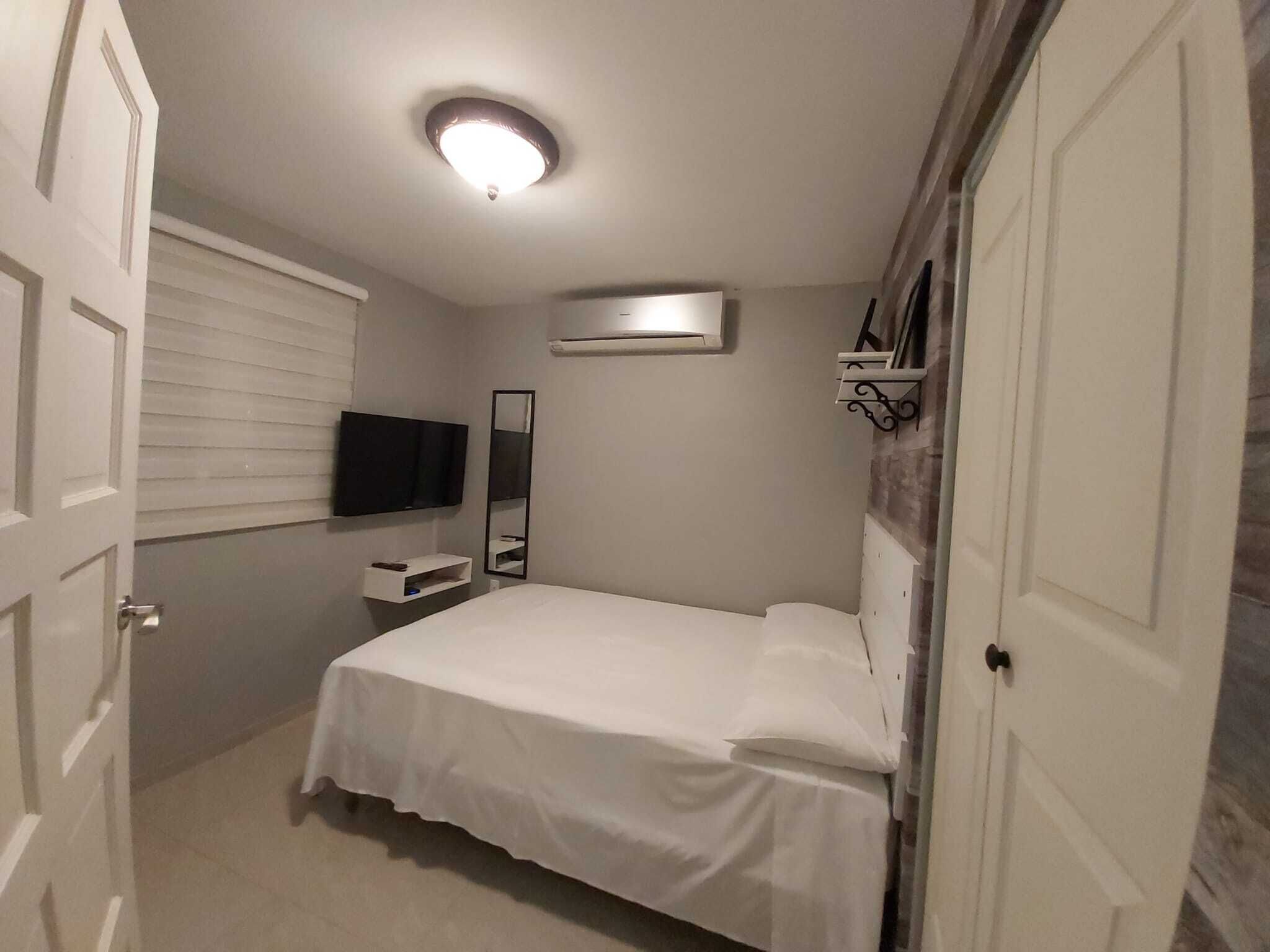Un dormitorio con cama, televisor de pantalla plana montado en la pared, mesita de noche y espejo.