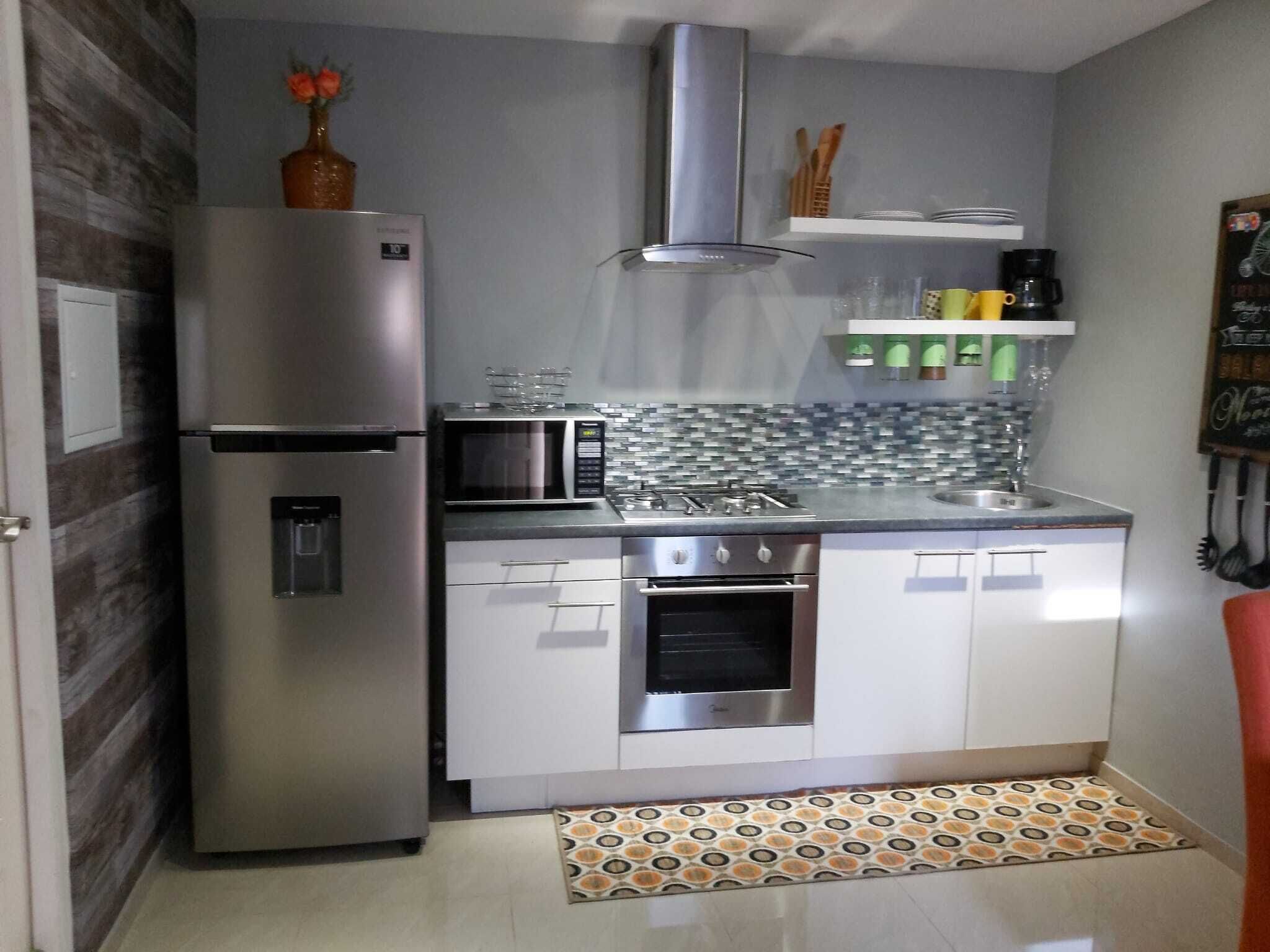 A compact kitchen with a refrigerator, microwave, oven, and a tiled backsplash.