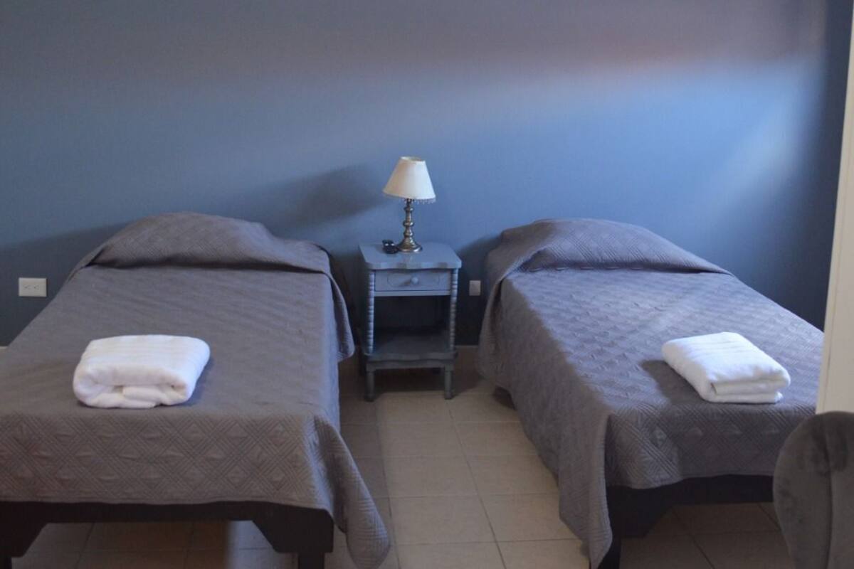 Una habitación con dos camas, una mesita de noche con lámpara y una silla.