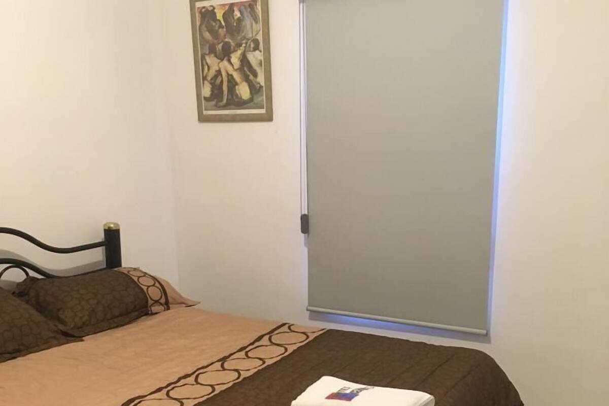 Un dormitorio con cama, armario, un cuadro y aire acondicionado.