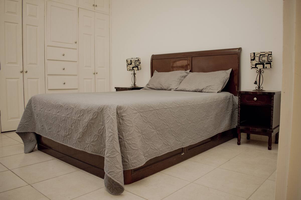 Una cama bien hecha con un cubrecolchón acolchado, un cabecero de madera y dos mesitas de noche con lámparas.