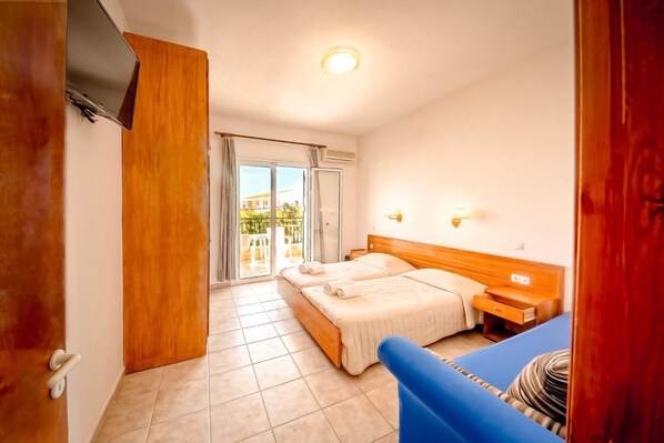 A hotel room with two beds, a TV, a wooden wardrobe, a balcony, and a blue sofa.